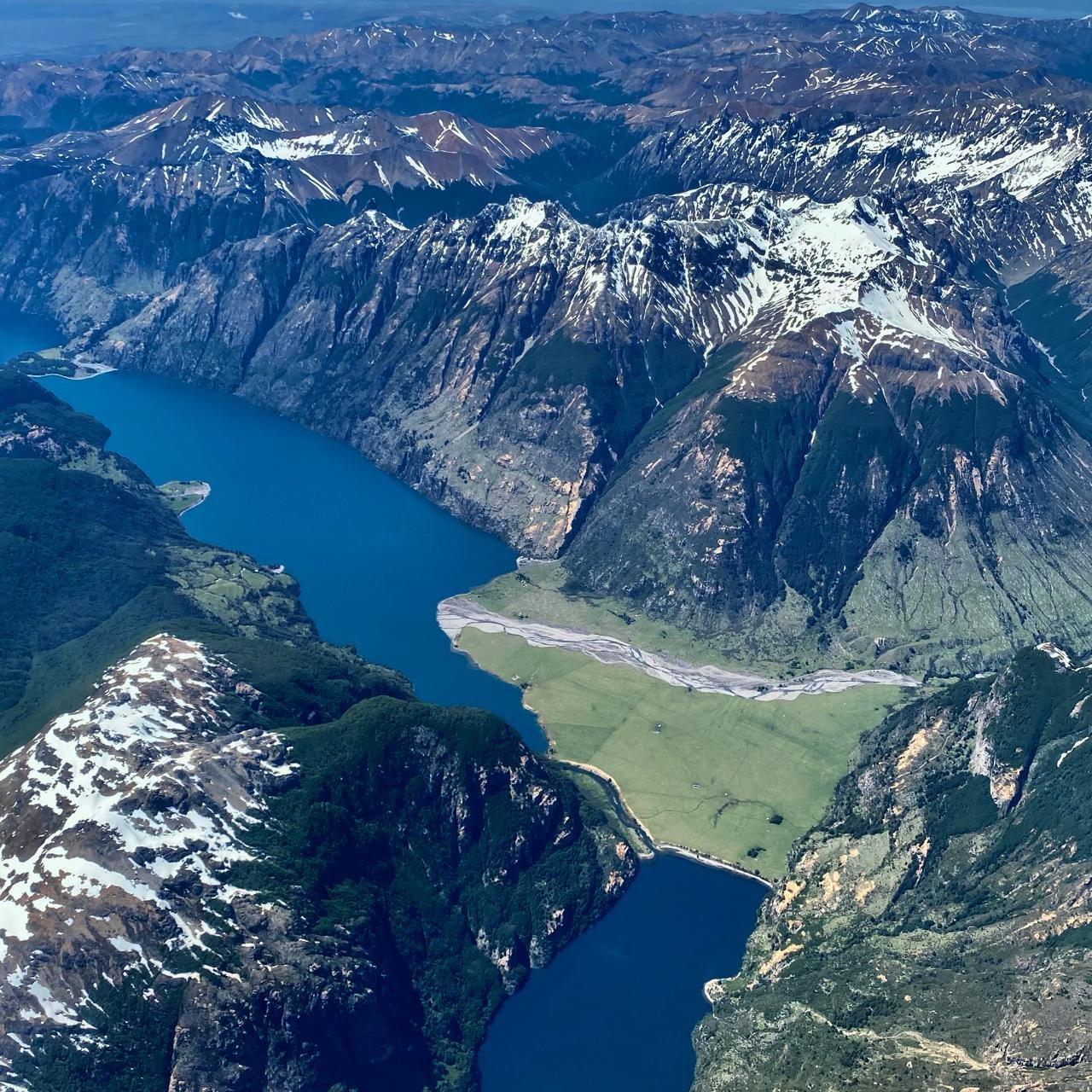 Vista aérea de un lago entre montañas nevadas y una pradera en su orilla